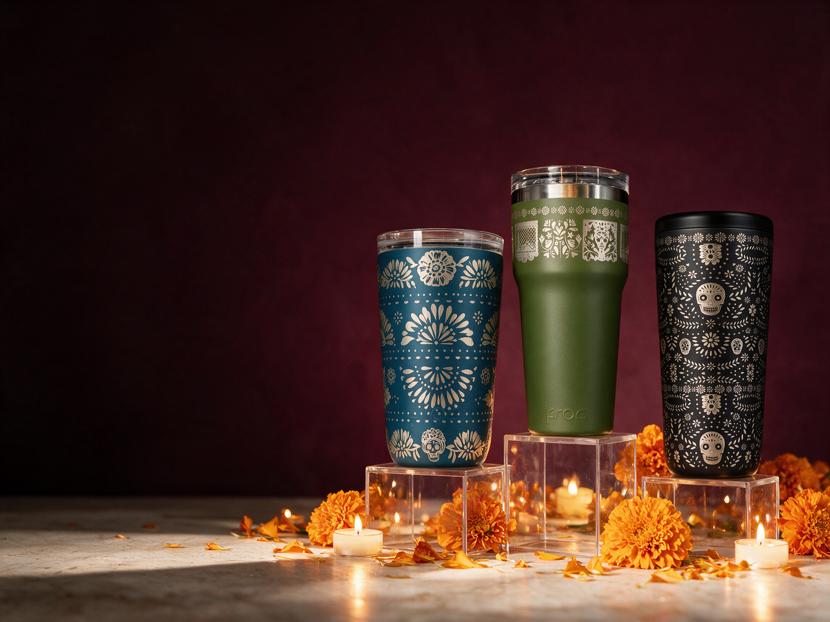 Colección Eterna FROC de termos grabados para Día de Muertos en azul, verde y negro, acompañados de flores de cempasúchil y velas sobre pedestales transparentes.